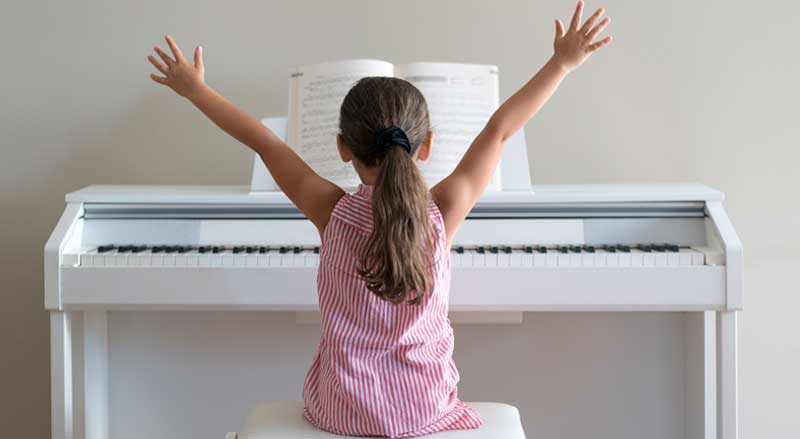 A young girl sitting at the piano with her arms raised in triumph