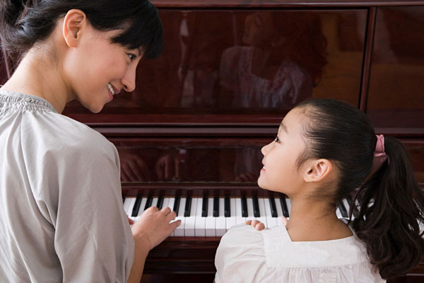 Woman teaching girl to play piano