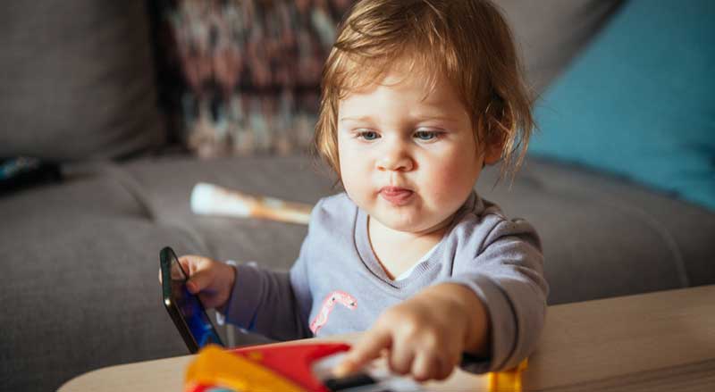 Baby holding phone and pressing down a key on a toy piano