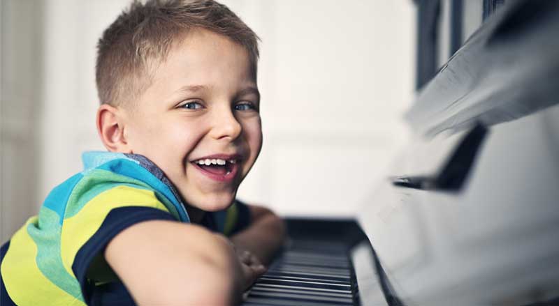 Boy smiling and leaning on piano keys