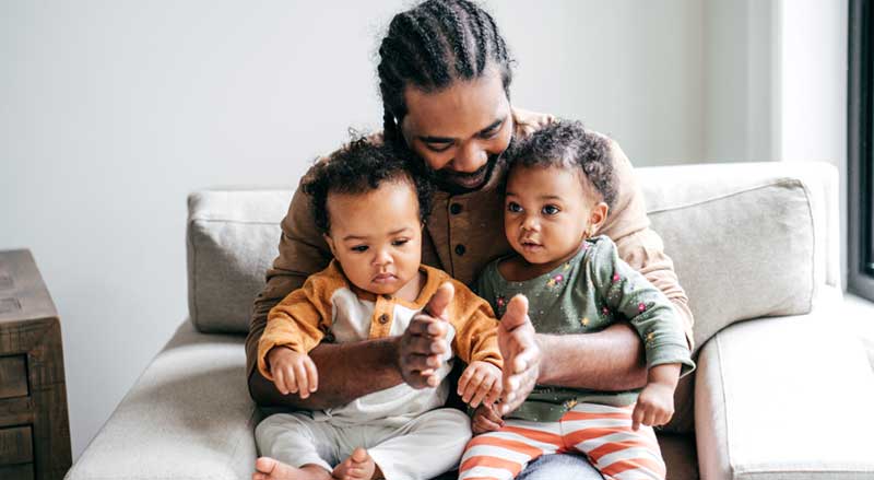 Man sitting with two children playing patty cake