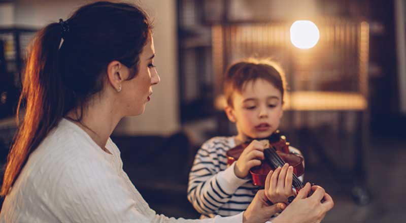 Woman showing young boy how to hold the violin