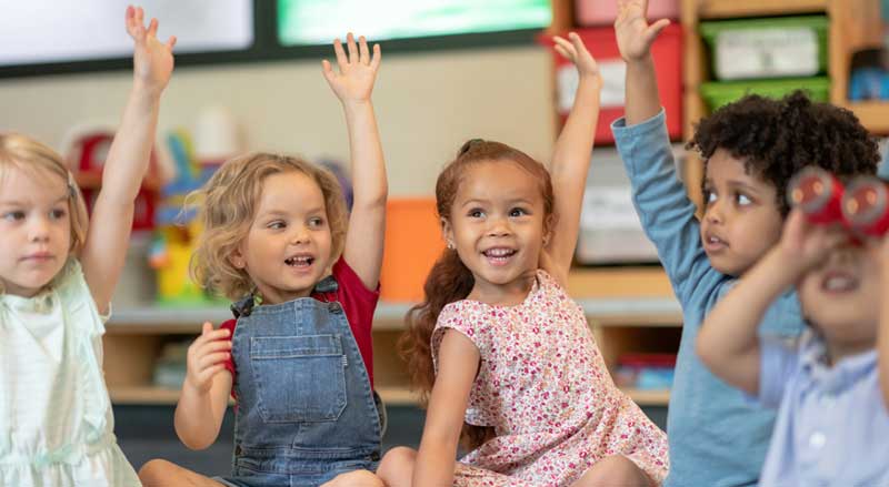 Young toddler students raising their hands at school