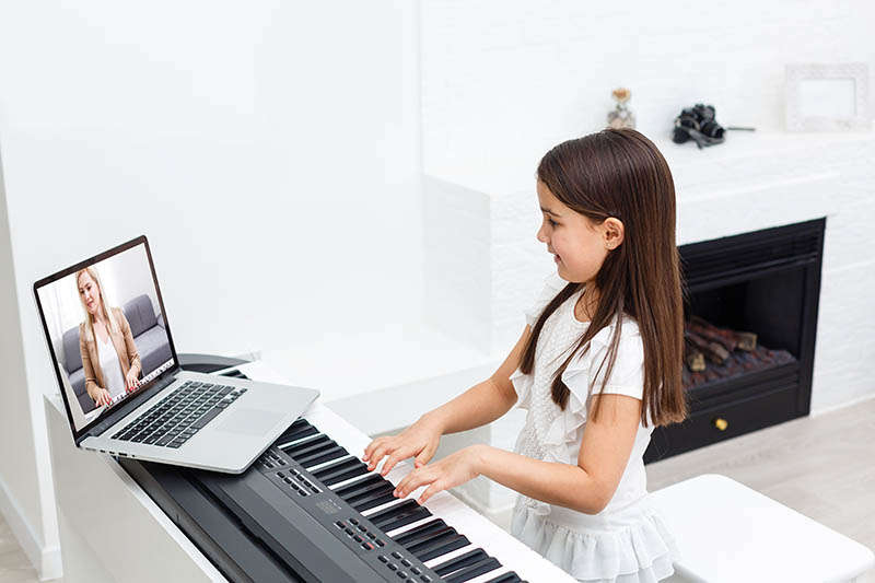 A young girl at a keyboard is taking an online piano lesson