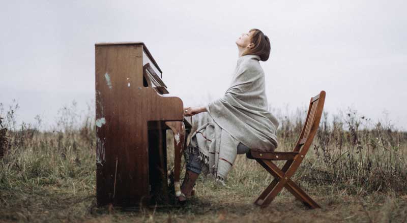 A woman sitting on a chair playing a piano outside in an open field