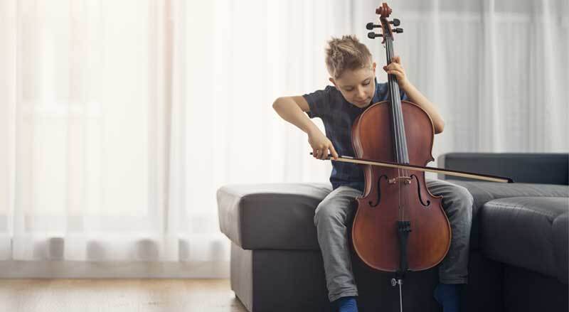 A boy is playing his cello at home.