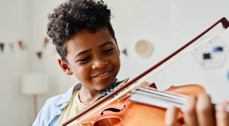 A smiling boy practicing his violin.