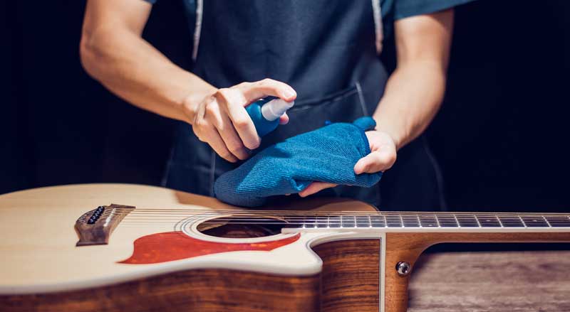 Close-up of a guitar and someone spraying guitar cleaner on a cloth