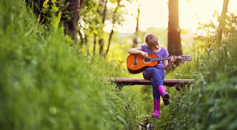 A young girl playing a guitar on a forest trail
