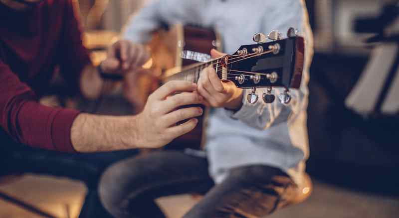 A boy is learning how to play the guitar and is receiving instruction from his music teacher