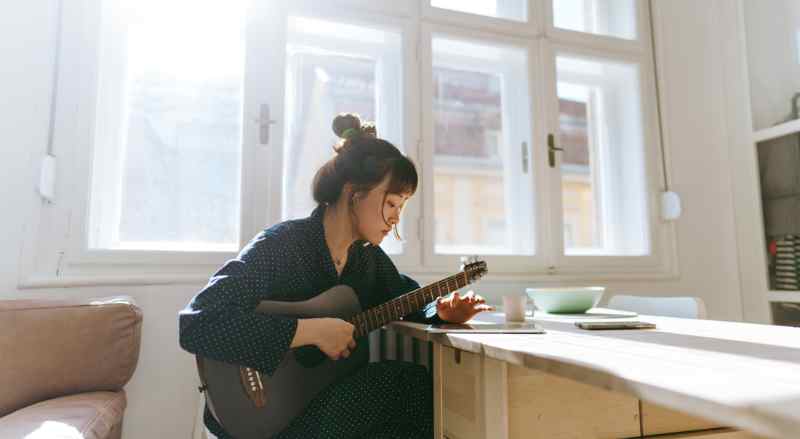 A woman is sitting in her home and is practicing playing the guitar