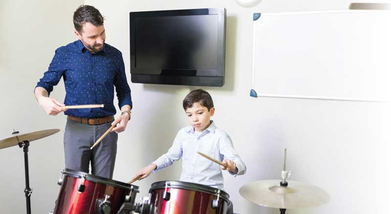 A drum teacher guiding a young boy playing drums