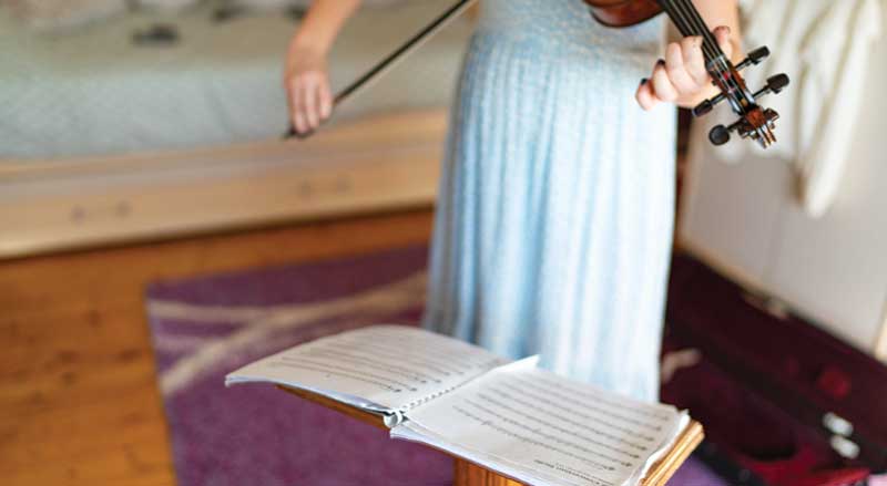 A young girl in a blue dress playing violin with sheet music on a stand