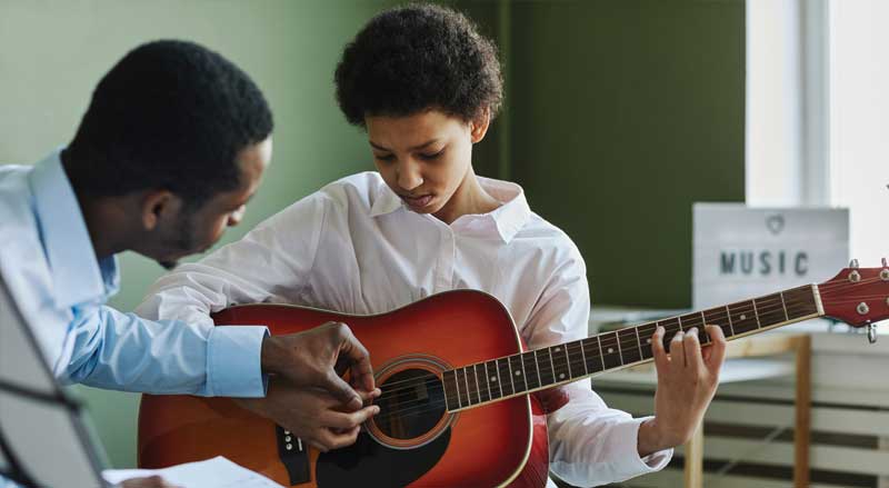 Music teacher guiding a young student playing guitar in classroom