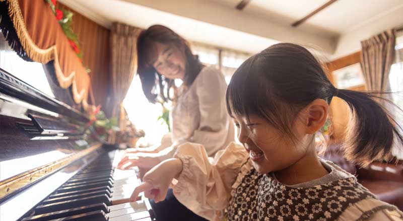 Young girl and her mother playing piano together at home