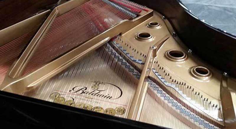 Close-up of the interior of a Baldwin grand piano, highlighting the brand logo, gold harp, and high-quality string construction.