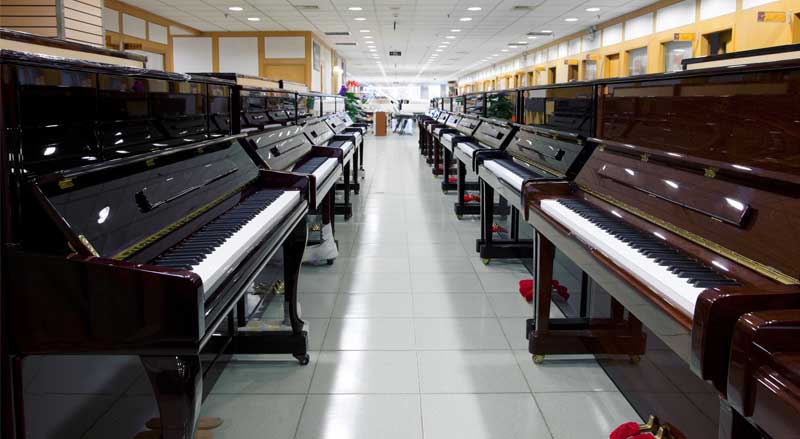 Showroom row of polished upright pianos displayed for sale, lined on both sides of a bright, spacious store
