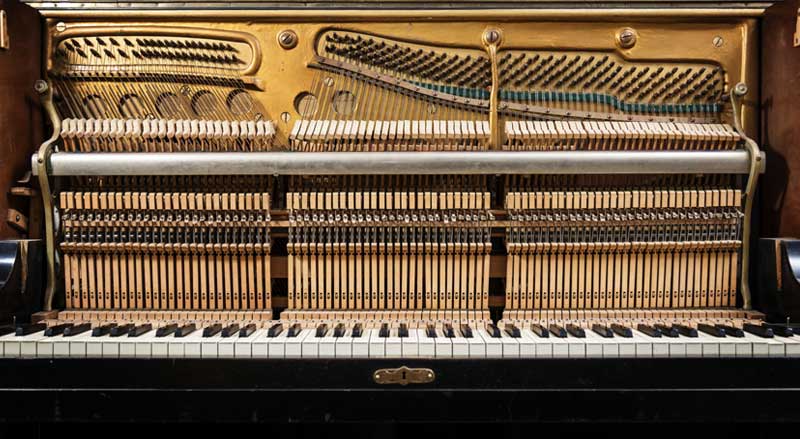 Interior view of an upright piano with action and strings exposed, displaying hammer mechanisms and tuning pins