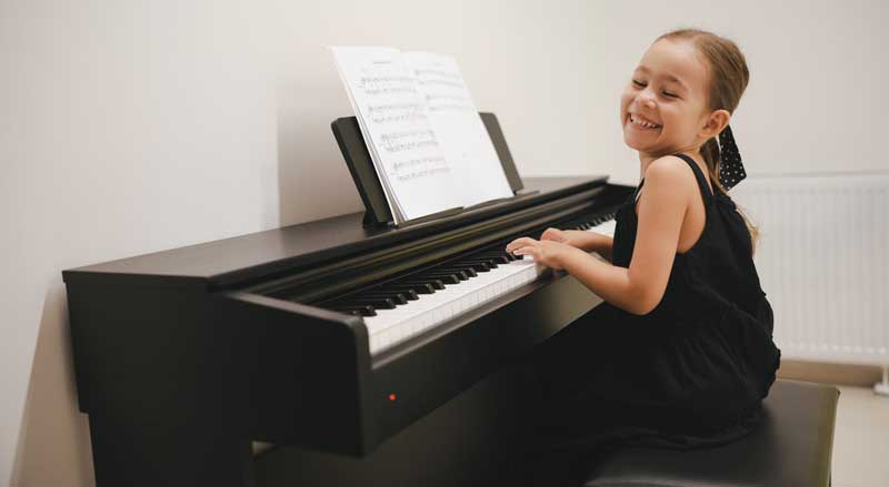 Young child smiling while practicing piano with sheet music, celebrating progress