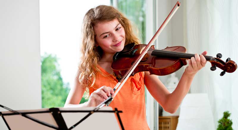 Student practicing violin while reading sheet music, focusing on building consistent music practice habits